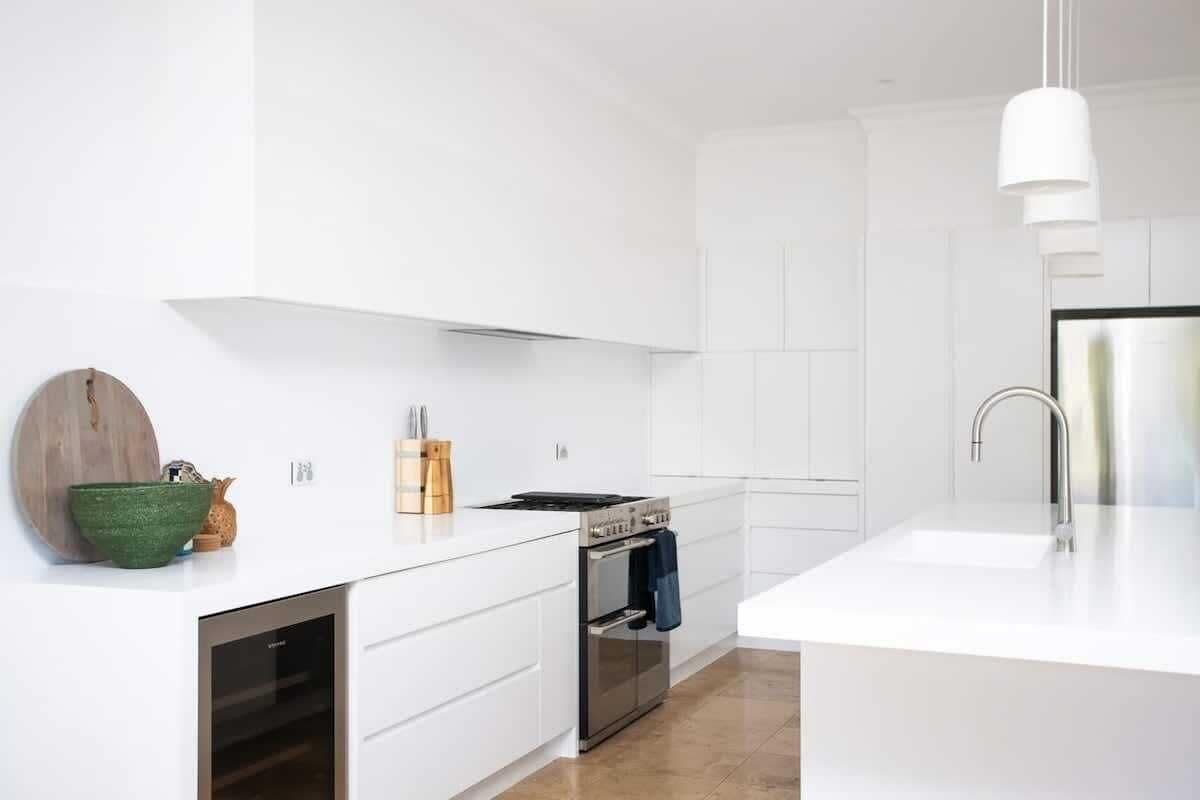 A modern kitchen with white cabinetry, a built-in oven, and a stainless steel sink.