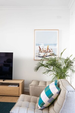 A living room with a television on a wooden stand, a beige sofa with a striped pillow, and a framed picture of a beach scene on the wall. - Casa De Palmeras (CASUARINA)