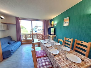 A dining area with a table set for four, a blue sofa, and a view of houses through a large window.