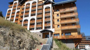 Ein mehrstöckiges Hotel mit Balkonen, einer Treppe, die zum Eingang führt, und blauem Himmel.