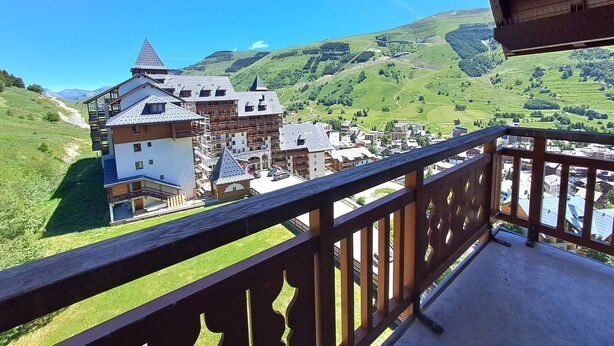 Eine Berglodge mit Balkon, Blick ins Tal und blauem Himmel.