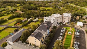 A residential area with a row of townhouses, a parking lot, and a beach in the background.