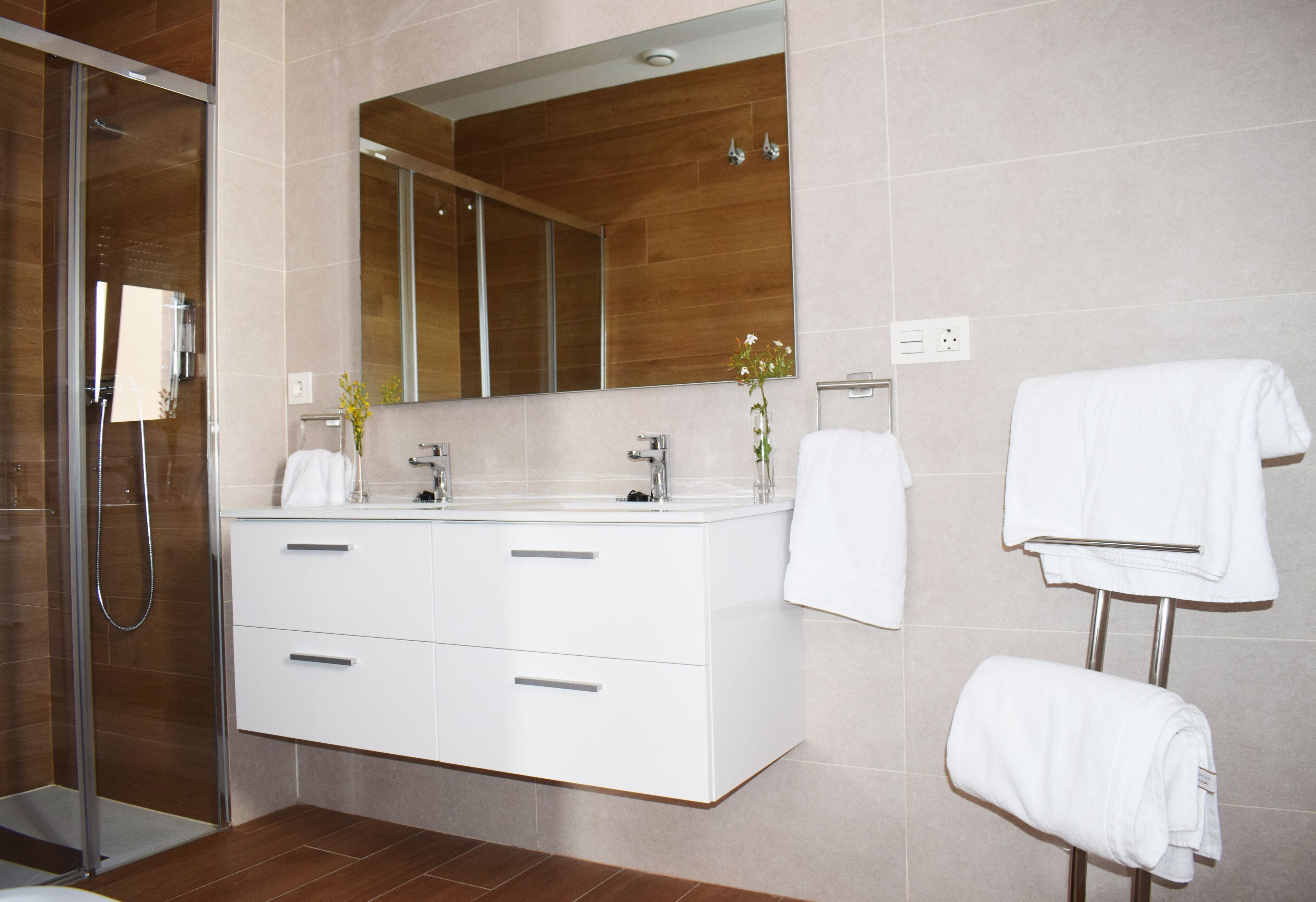 A modern bathroom with a large mirror, two sinks, a shower, and white towels.