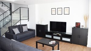 A modern living room with a grey sofa, a black entertainment unit with a flat-screen TV, and a staircase with glass railings. - Magnificent house with private pool in Granada (Granada)