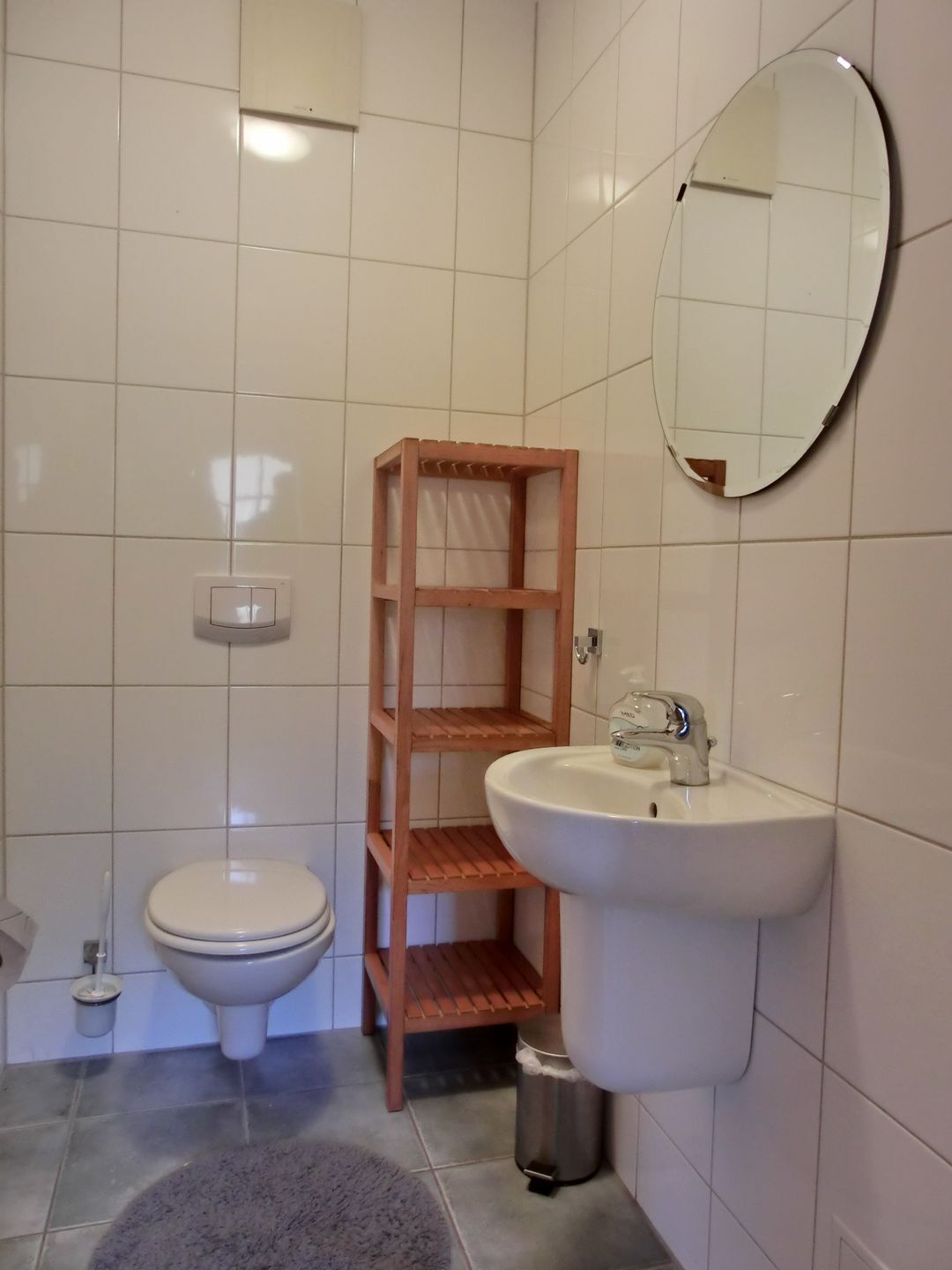 Une salle de bain comprenant des toilettes, une étagère en bois, un lavabo et un miroir.