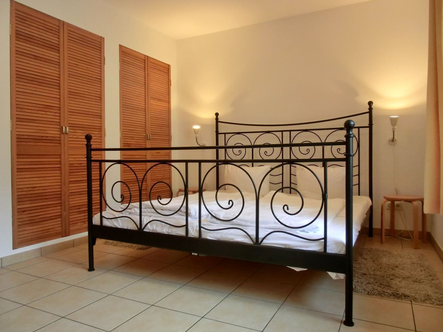 Een kamer met een bed met metalen frame, houten schuifdeuren en een klein nachtkastje.