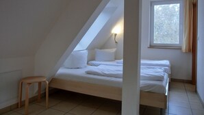 A small, single-bed room with a sloped ceiling, a window with curtains, and a bedside lamp. - 2-room vacation apartment for 4 people on the 1st floor - with WLAN - NH (Ribnitz-Damgarten)