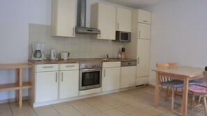 A compact kitchen with a stove, microwave, and cabinets. There is a wooden table with chairs and a bench. - 2-room vacation apartment for 4 people on the 1st floor - with WLAN - NH (Ribnitz-Damgarten)