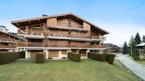 A multi-story wooden building with balconies, a paved driveway, and well-maintained hedges.