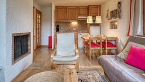 A cozy living room with a fireplace, a dining area with wooden furniture, and a kitchen with wooden cabinets and a modern pendant light.