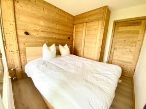 Ein Schlafzimmer mit einem Holzkopfteil, einem Bett mit weißer Bettwäsche und einer Holztür.