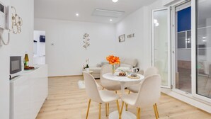 A modern dining area with a round table and four chairs, a white cabinet with a television, and a large window with a view.