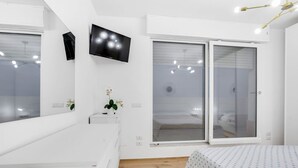 A modern bedroom with a bed, a TV, a sliding door, and a small plant.