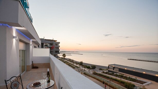 A balcony with a table, chairs, and a bottle of wine.