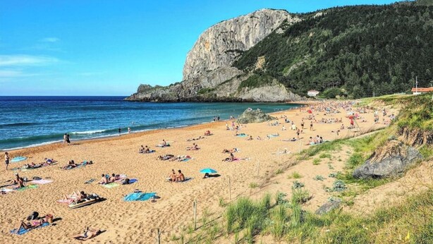 A beach with people sunbathing and swimming, a rocky cliff, and a clear blue sky. - Piso Céntrico y Tranquilo en Gernika (Gernika-Lumo)