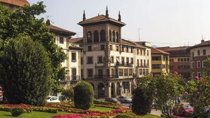 A historic building with a central tower, surrounded by lush gardens and parked cars. - Piso Céntrico y Tranquilo en Gernika (Gernika-Lumo)