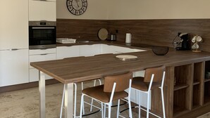 Une cuisine moderne avec un îlot central en bois, des chaises blanches et une horloge au mur.