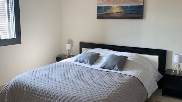 Une chambre à coucher avec un lit, deux tables de chevet, une commode, une fenêtre et un tableau au mur.
