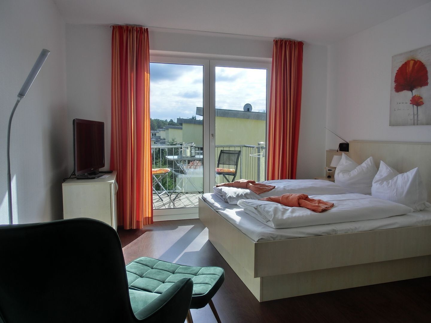 Habitación de hotel con cama, una silla, escritorio con lámpara y vistas al exterior.