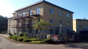 Un immeuble à plusieurs étages, doté d’escaliers extérieurs, d’un petit arbre et d’une clôture.
