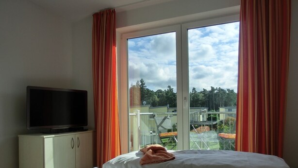 Une chambre d’hôtel avec un lit, un téléviseur posé sur un meuble et un balcon équipé d’une table et de chaises.