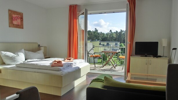 A hotel room with a bed, a television, a desk, and a balcony with a table and chairs. - KW21 "Südwind 2" - 1-room apartment for max. 2 persons, WLAN (Gelbensande)