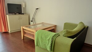 A living room with a green sofa, a wooden coffee table, a television on a cabinet, and a floor lamp. - KW21 "Südwind 2" - 1-room apartment for max. 2 persons, WLAN (Gelbensande)
