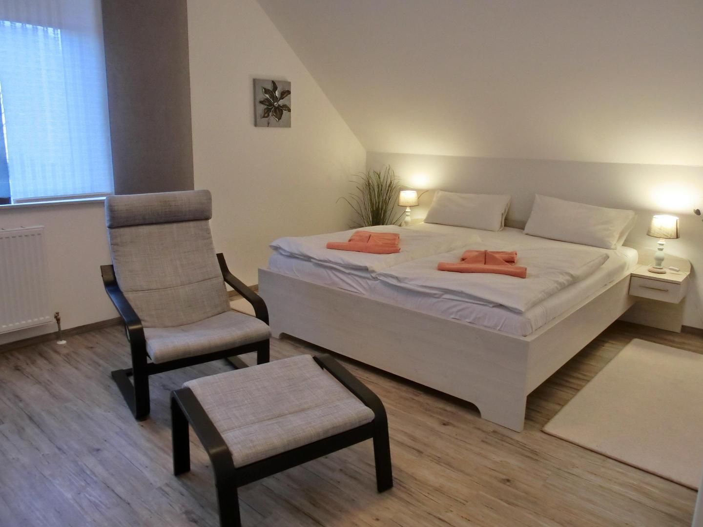 A bedroom with a bed, two chairs, a nightstand, and a small plant.