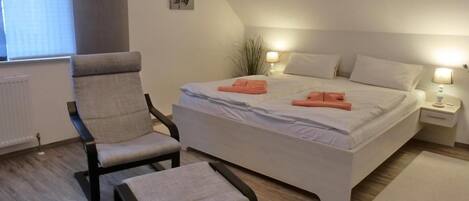 A bedroom with a bed, two chairs, a nightstand, and a small plant.