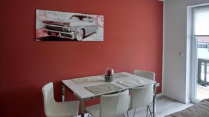 A dining area with a table and chairs, a painting on the wall, and a window with a view.