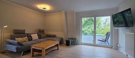 A modern living room with a grey sofa, a wooden coffee table, and a TV mounted on the wall.