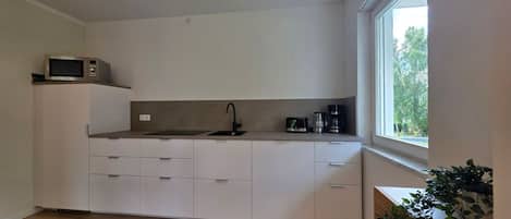 Una cocina compacta con microondas, cafetera y lavamanos.