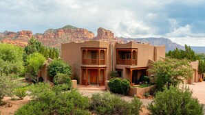 A two-story building with wooden balconies, surrounded by greenery and set against a mountainous backdrop. - Gated Historic Estate • Pool, Spa & Artifacts (Sedona)