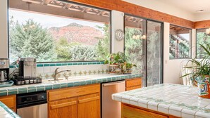 A kitchen with wooden cabinets, a coffee machine, and a view of red rock formations. - Gated Historic Estate • Pool, Spa & Artifacts (Sedona)