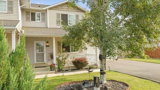 A two-story house with a front porch, a small garden with a tree and shrubs, and a clear driveway. - Charming Townhouse in the River Road Neighborhood - Pet friendly - Close to Downtown (Missoula)