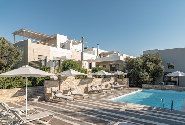 A modern pool area with lounge chairs and umbrellas, stone walls, and a clear blue sky. - Eco Villa, Serene Nature Retreat Near the Beach (Rethymno)