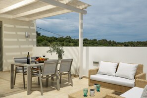 A covered outdoor dining area with a table and chairs, a wicker sofa, and a view of the landscape. - Eco Villa, Serene Nature Retreat Near the Beach (Rethymno)
