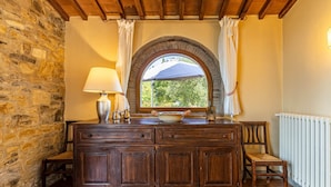 Un mur en pierre rustique, un meuble en bois avec des tiroirs, une lampe de table, un bol et une chaise.