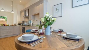 Una cucina moderna con mobili bianchi, un tavolo da pranzo in legno apparecchiato per quattro persone e un vaso di fiori sul tavolo.