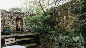 A stone wall with a statue, a bench, and a table in a garden setting.