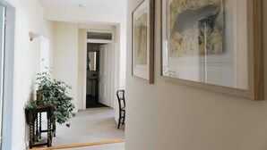 A hallway with framed artwork on the walls, a potted plant, and a chair.