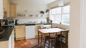 A kitchen with a stove, microwave, and dishwasher, wooden cabinets, a window with a view, and a table with chairs.