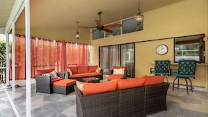 Un patio couvert aménagé avec des meubles en osier, un ventilateur de plafond et une horloge murale.