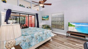 Une chambre à coucher avec un lit, un ventilateur de plafond, une télévision et une fenêtre donnant sur la plage.