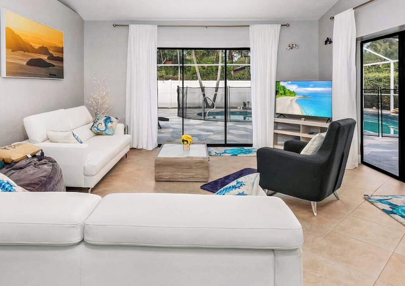 A modern living room with a white sofa, a black armchair, a coffee table, and a large window overlooking a pool.