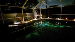 Une vue nocturne d’une piscine dotée d’une enceinte en verre, entourée de lumières et d’un petit bateau.