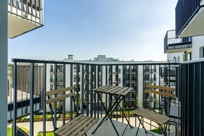 A balcony with a wooden table and benches, overlooking a courtyard with greenery and modern buildings.