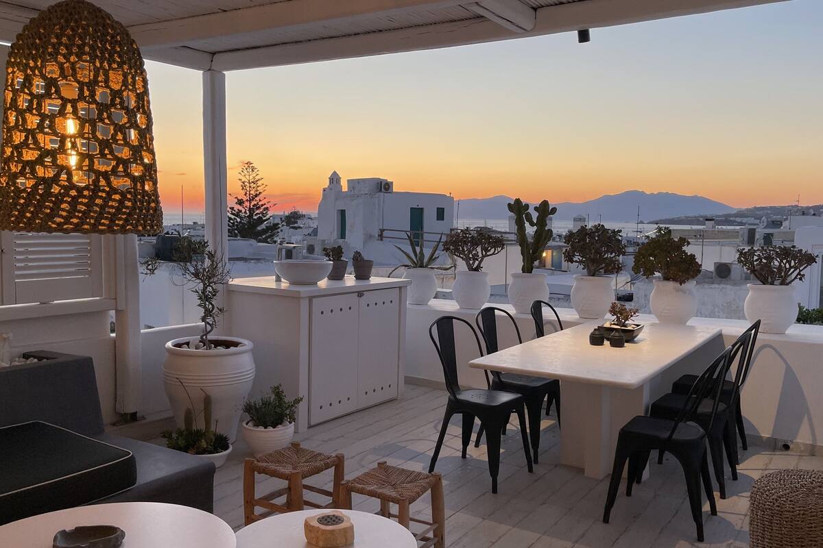 A terrace with a dining table, chairs, potted plants, and a hanging light fixture.