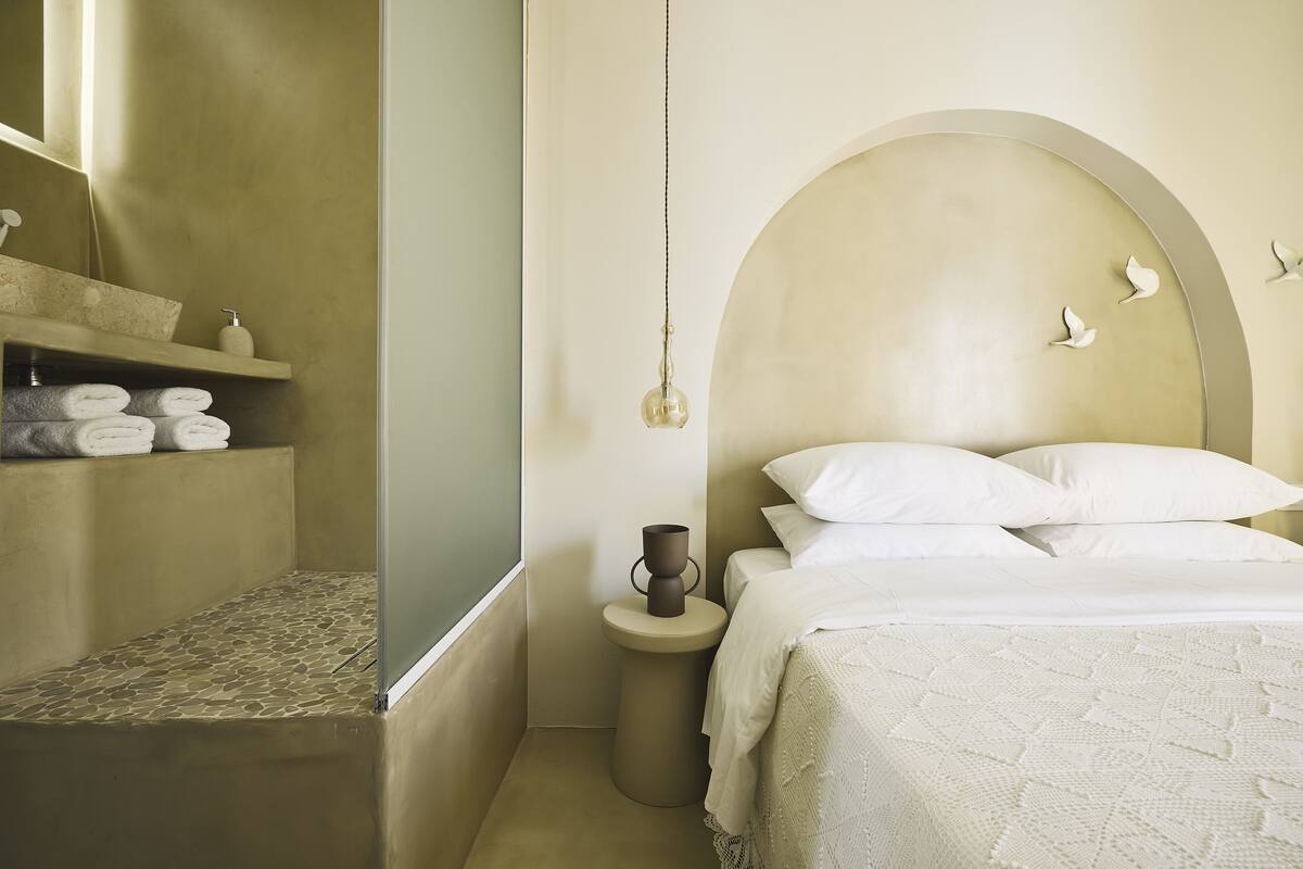 A bedroom with a bed, a bedside table, a nightstand, a mirror, and a window.