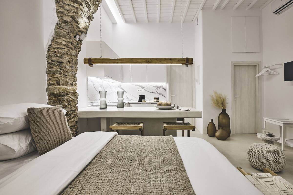 A modern bedroom with a stone accent wall, a large mirror, a bed with white linens, and a bedside table with decorative items.